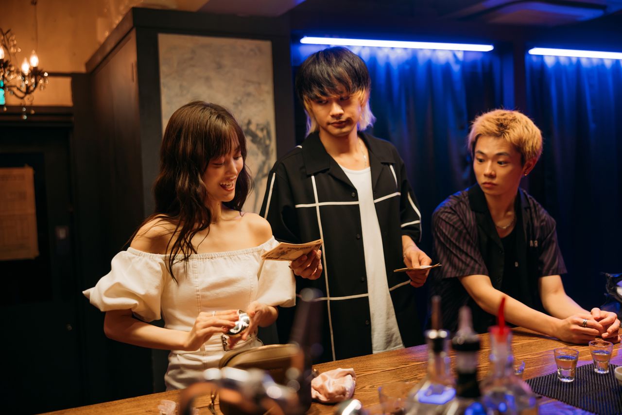 يدفع تاكويا مبلغًا من المال لكيسارا (ياماشيتا ميزوكي)، إحدى النساء اللواتي أُرسلن لإقناع أهداف مامورو بالبيع (© 2025 شركاء فيلم هوية الأحمق)