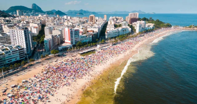 ساحل البرازيل ويجلس على الشاطىء مصطافين كثيرون وفي الخلف بنايات حديثه.