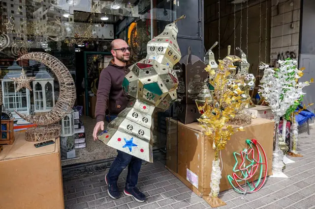 رجل يحمل فانوساً ضخماً أمام متجر في مدينة الخليل في الضفة الغربية