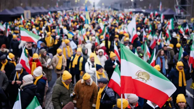 يرفرف علم إيراني يعود لما قبل الثورة بينما يقف الناس جنباً إلى جنب خلال مسيرة تضامنية مع الشعب الإيراني أمام بوابة براندنبورغ في برلين، ألمانيا، 7 فبراير/شباط 2026. 
