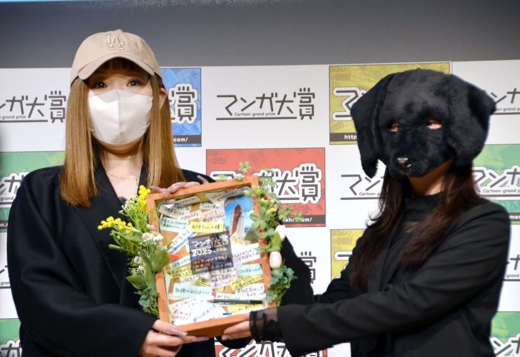 أورينو كيكو مؤلفة مانغا ”أليس، دوكو مادي مو“ (على اليسار)، تتسلم جائزة مانغا تايشو عام 2025، وهي جائزة يختارها موظفو المكتبات في جميع أنحاء اليابان، من الفائز بالجائزة العام الماضي دورونودا إينوهيكو (© كيودو).