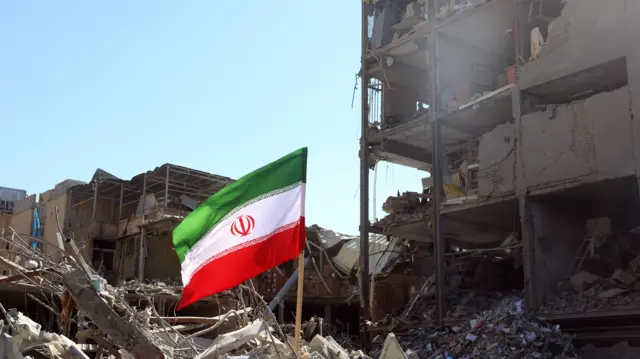 علم إيراني رفع بجوار مبنى متضرر في ساحة الفردوسي بعد غارة جوية في وسط طهران، إيران، في 3 مارس/ آذار 2026.