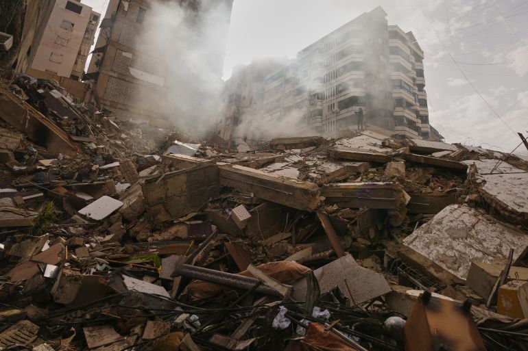 A man stands atop the rubble of a building destroyed in an Israeli airstrike as a bulldozer clears debris in Dahiyeh, Beirut's southern suburbs, Lebanon, Saturday, March 14, 2026. (AP Photo/Hassan Ammar)
