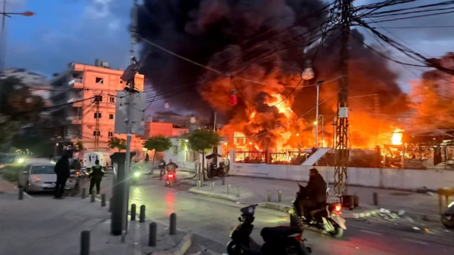 إيرانيون يمرون ليلاً من أمام موقع انفجارات ضخمة حيث تشتعل النيران ويتصاعد الدخان في العاصمة طهران