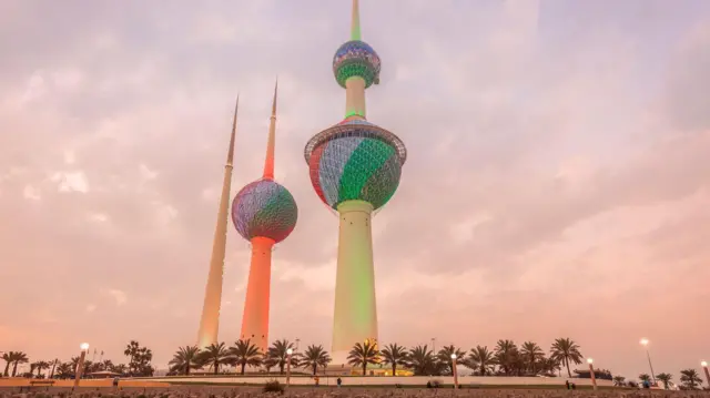 صورة لأبراج الكويت عند المغيب وهي مضاءة بعلم الكويت.