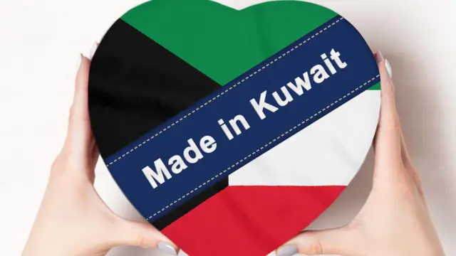 صورة تظهر يدَيْ امرأة تحمل علبة على شكل قلب وبألوان العلم الكويتي.