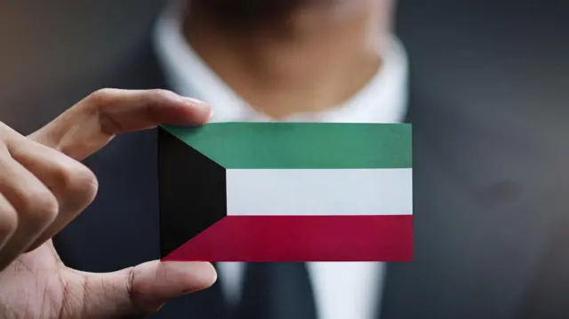 صورة لرجل أعمال يحمل بطاقة على شكل علم دولة الكويت في يده.