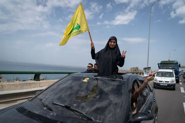 سيدة تلوّح بعلم حزب الله بينما يسير الناس نحو جنوب لبنان في اليوم الأول بعد اتفاق وقف إطلاق النار في 17 أبريل/نيسان ٢٠٢٦ شمال صيدا في الرميلة، لبنان