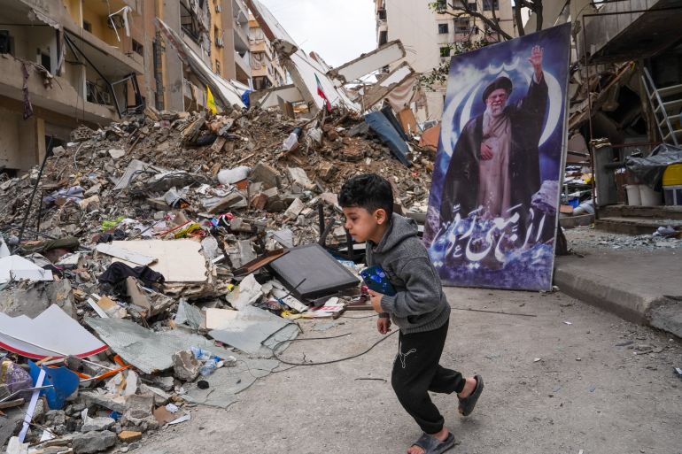 BEIRUT, LEBANON - APRIL 20: A boy runs past a poster of former Supreme Leader of Iran, Ali Khamenei near the rubble of a building that was damaged by an Israeli air-strike in Beirut's southern suburb of Dahieh, on April 20, 2026 in Beirut, Lebanon. At 00:00 on April 17, a 10-day ceasefire took effect that is meant to pause fighting between Israeli forces and the Lebanese militant group Hezbollah. The agreement was announced the night before by U.S. President Donald Trump and described as a ceasefire between Israel and Lebanon; Hezbollah acknowledged the ceasefire but did not directly confirm it would abide by it. (Photo by Ryan Murphy/Getty Images)