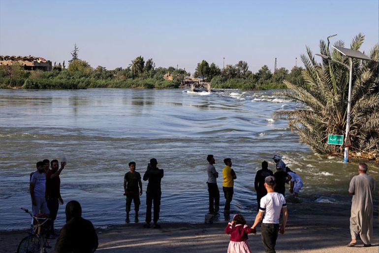 People stand at the site of a collapsed bridge while they wait for assistance to cross to the other side in Syria's Deir Ezzor province as water levels from the Euprates river rise on May 30, 2026. Syria's energy ministry warned on April 28 of rising water levels on the Euphrates River after flooding in the north and east following increased flows from neighbouring Turkey and recent rains. A statement said government water authorities in Deir Ezzor, Raqa and Aleppo provinces had announced a "state of emergency" and were taking precautionary measures. (Photo by Bakr ALKASEM / AFP via Getty Images)