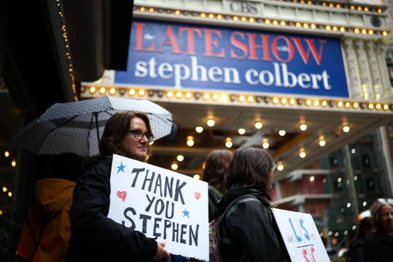 People hold signs supporting Stephen Colbert outside the Ed Sullivan Theater ahead of the taping of the final episode of the "The Late Show" after 32 years on air, in New York, on May 21, 2026.