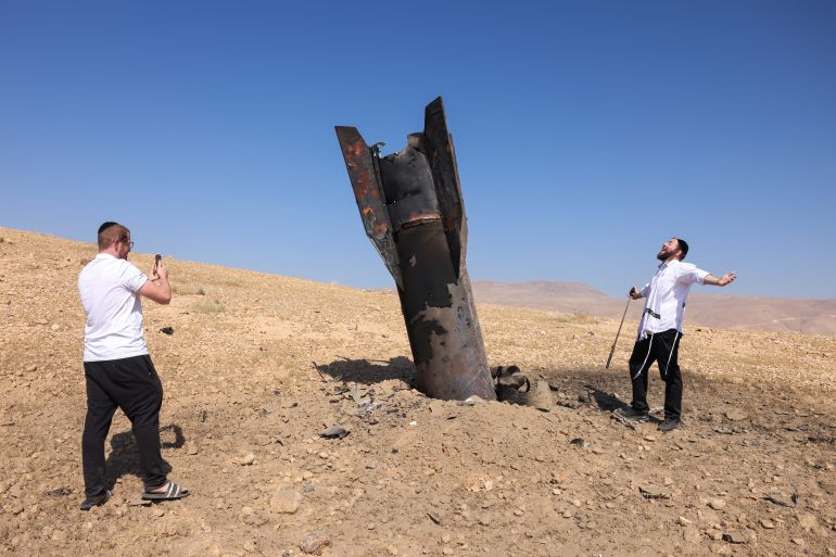 TOPSHOT - A man poses for a photo next to a fallen rocket half-buried in the ground on the outskirts of Jericho on June 8, 2026, following Iranian and Iran-backed Houthi rebel attacks.