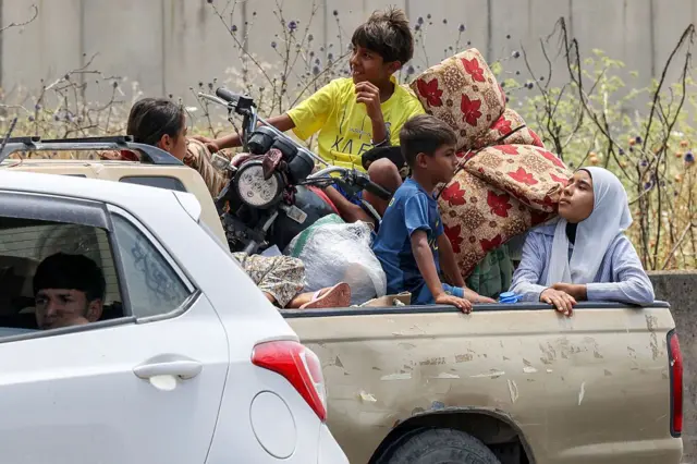 أطفال يجلسون في صندوق شاحنة صغيرة منتظرين وسط زحام المرور، وبجوارهم داخل صندوق الشاحنة أغراضهم.