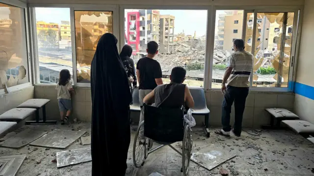 صورة لعائلة من ضمنها شخص على كرسي متحرك، بجوار نافذة مستشفى جبل عامل. في الخارج زجاج متناثر والأنقاض على أرضية غرفة المستشفى التي يقفون فيها، في مدينة صور يوم الاثنين.