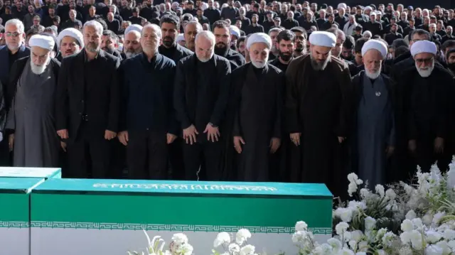 يؤدي مسعود بزشكيان، ورئيس البرلمان الإيراني محمد باقر قاليباف، ورئيس السلطة القضائية الإيرانية غلام حسين محسني إيجئي، إلى جانب مسؤولين آخرين، صلاةً خلال مراسم الوداع الشعبية تكريماً للمرشد الأعلى الراحل علي خامنئي. ويظهر في الخلفية حشد كبير من المشيعين وهم يقفون متجهين بأنظارهم نحو النعش.