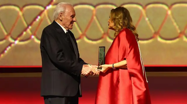 يسرا الممثلة المصرية (يمين) بثوب أحمر تقدم جائزة لأنتوني هوبكينز - بزة رسمية سوداء