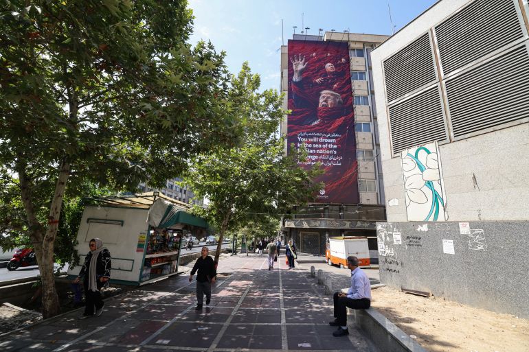 People walk in front of a huge anti-US and Israel billboard featuring US President Donald Trump and Israel's Prime Minister Benjamin Netanyahu in Tehran on July 19, 2026.
