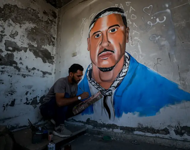 فنان فلسطيني يرسم جدارية تكريماً لمغني الراب الأمريكي ماكليمور داخل مبنى تضرّر خلال الحرب في مدينة غزة.