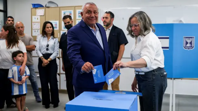 زعيم حزب يشار غادي أيزنكوت يدلي بصوته بمرافقة سيدة وخلفه أشخاص في مركز التصويت